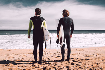 Two surfers are looking at the ocean and waiting a big  wave