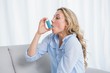 © WavebreakMediaMicro - Blonde using her asthma inhaler on couch