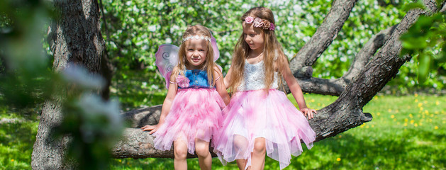 Wall Mural - Little adorable girls sitting on blossoming tree in apple garden