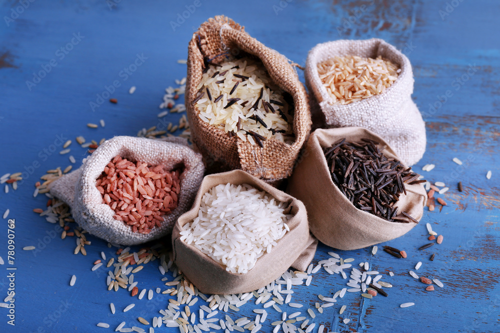 Different types of rice in sacks on wooden background