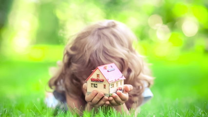 Wall Mural - Happy child holding model house in spring park. Slow motion