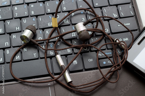 Fotografie, Obraz Tangled headphones and cell phone at the keyboard.