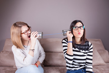 blonde and brunette women talking with tin can telephone