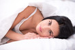 © Friends Stock - Dark haired woman is under a blanket looking at camera