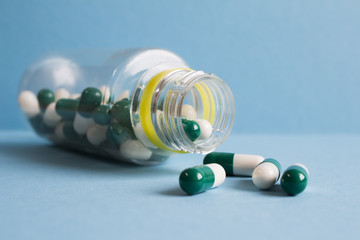 Green and white pills spill out of a plastic jar on blue backgro