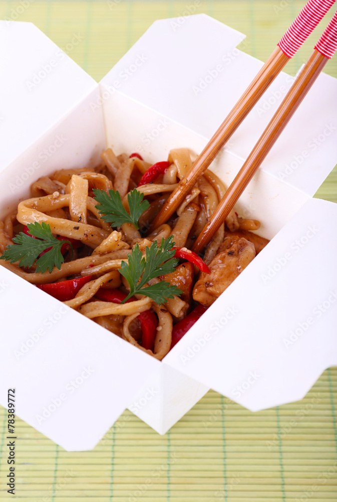 Fried noodles in takeaway box on mat background