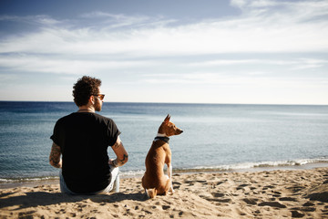 Caucasian man in sunglasses sitting in beach with friend’s dog