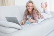 © WavebreakMediaMicro - Smiling blonde lying on couch shopping online