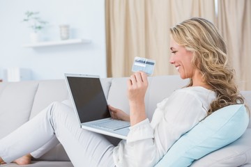 Wall Mural - Happy blonde sitting on couch shopping online