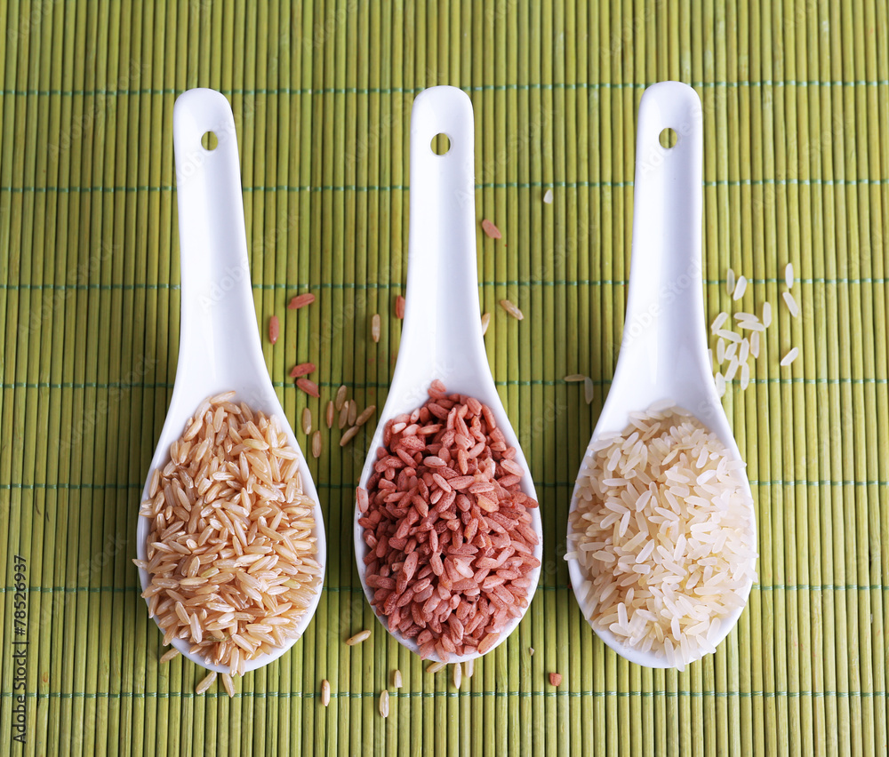Different types of rice in spoons on bamboo background