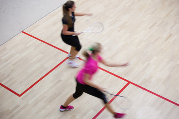 Two female squash players in fast action on a squash court