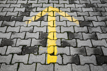 Yellow arrow painted on dark gray cobblestone pavement