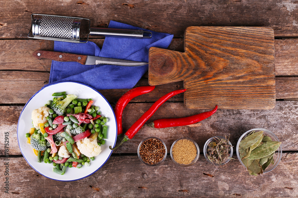Frozen vegetables and blank notebook, on wooden table