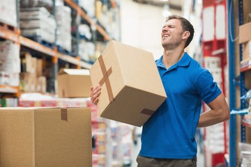 Worker with backache while lifting box in warehouse