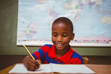 Cute little boy writing book in classroom