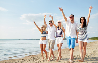 Wall Mural - smiling friends walking on beach and waving hands