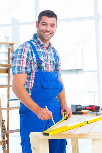 Fotografie, Obraz Smiling handyman using tape measure at workbench in office