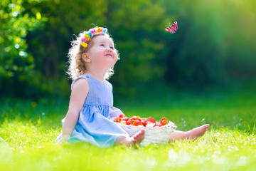 Wall Mural - Little girl eating strawberry watching a butterfly