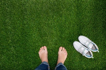 Canvas Print - Feet resting on green grass with sneakers