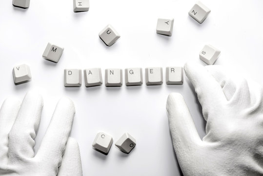Hands with gloves typesetting danger with white keys on white