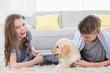 © WavebreakMediaMicro - Siblings playing with puppy on rug