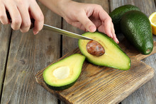 Young Woman Cuts Avocado On Cutting Board On Table Close Up