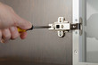 A man uses a screwdriver to adjust a concealed hinge fixed on a modern cabinet with a glass door