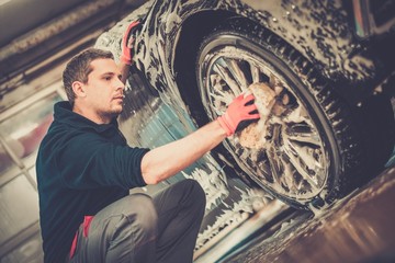 Poster - Man worker washing car's alloy wheels on a car wash