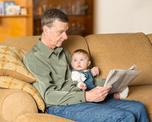 Young Baby Looking Up At Grandad With Paper