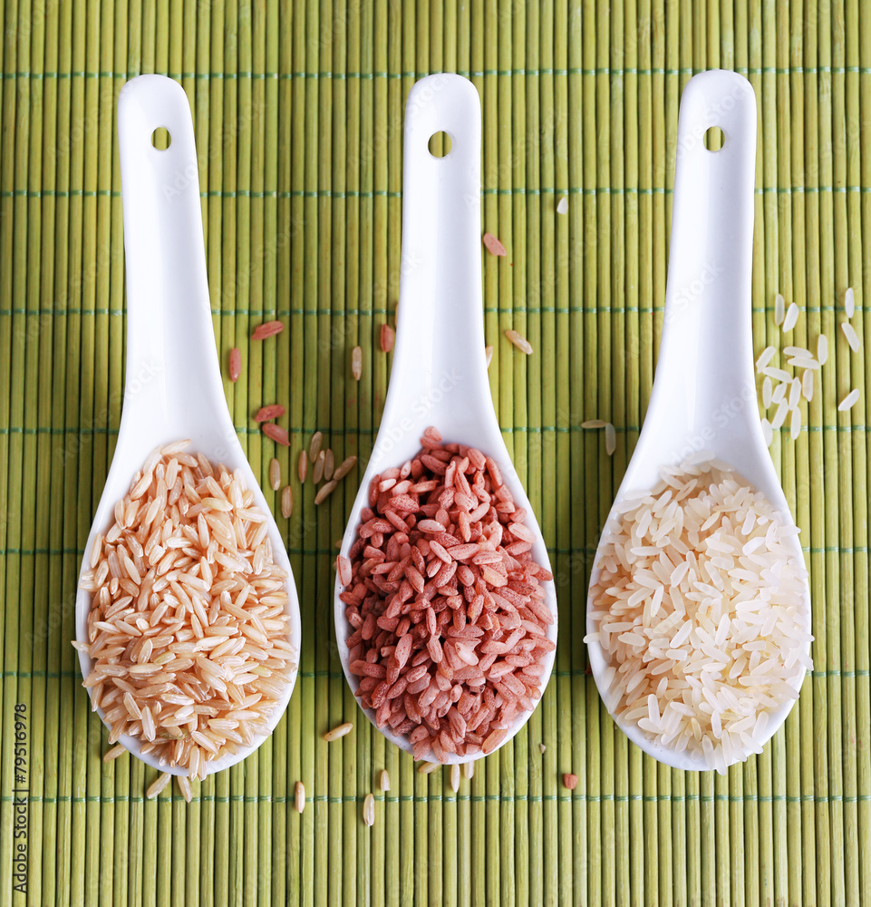 Different types of rice in spoons on bamboo background