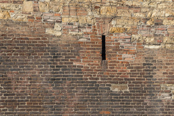 Old brick wall with wild stone and a narrow porthole