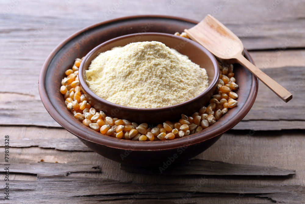 Flour and corn grains in bowls with spoon on wooden background
