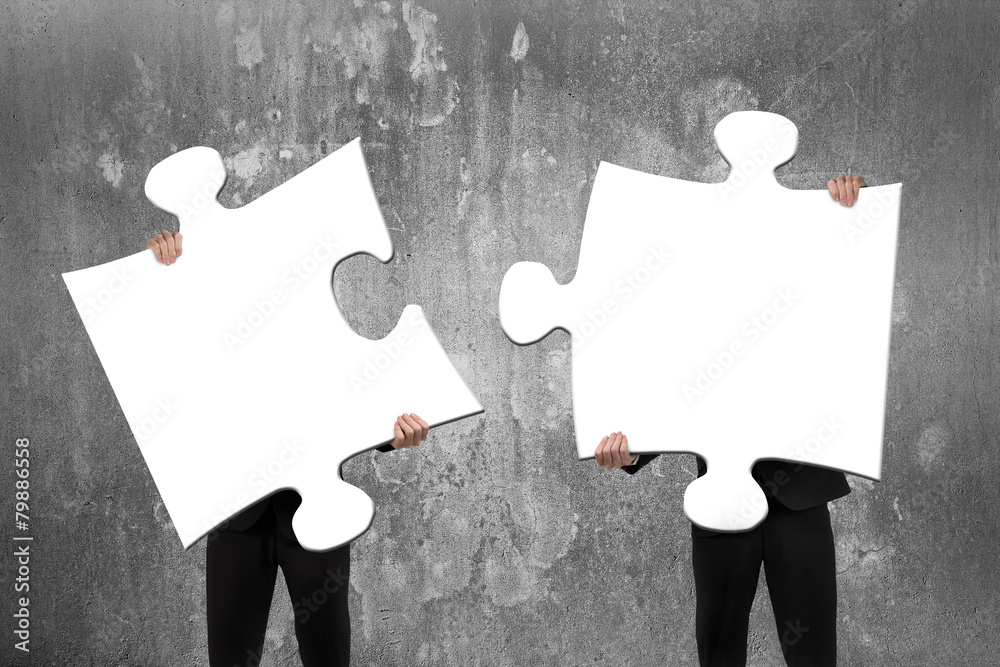Two business people assembling white jigsaw puzzles with concret - obrazy, fototapety, plakaty 