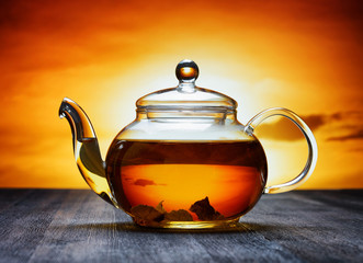 Canvas Print - Glass teapot of fresh aromatic tea on a black wooden table and o