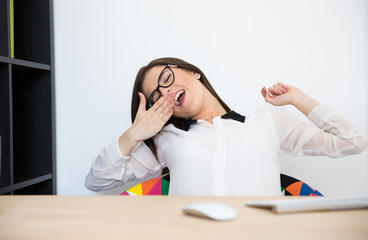 Canvas Print - Young businesswoman sitting at her workplace and yawning