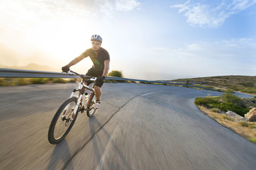 Wall Mural - Cyclist man riding mountain bike in sunny day on a mountain road