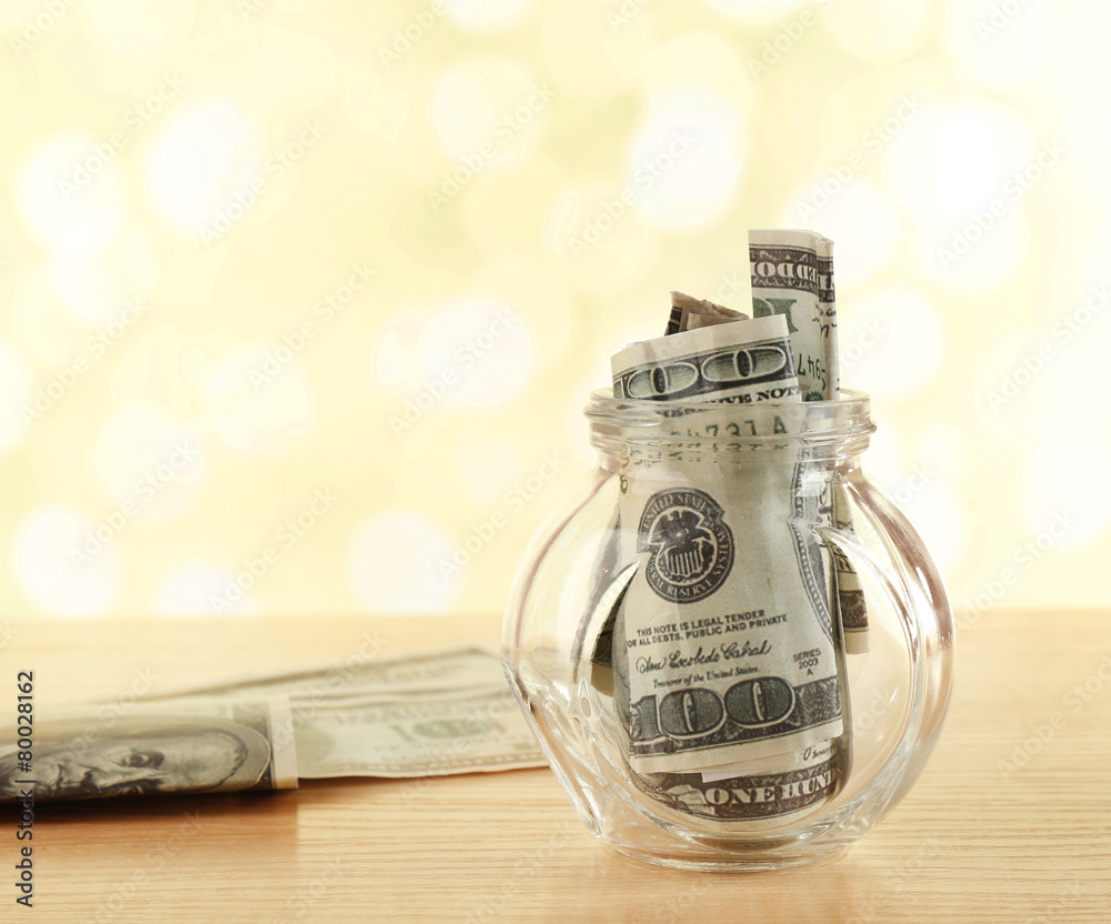 Dollars in glass bottle on bright blurred background