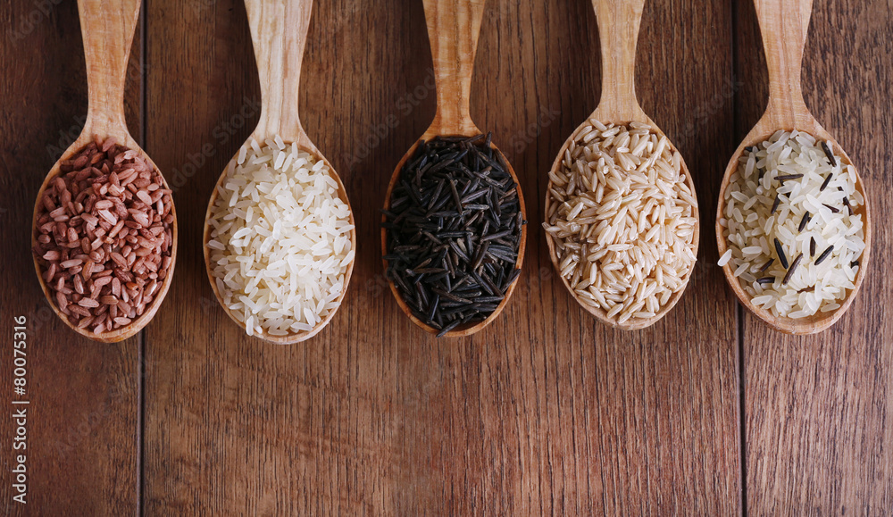Different kinds of rice in spoons on wooden background