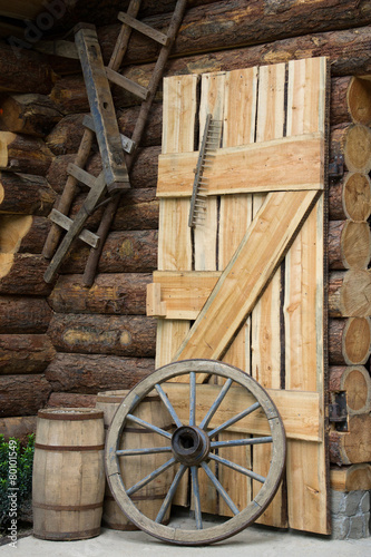 Obraz w ramie Log cabin with door, barrels and wheel