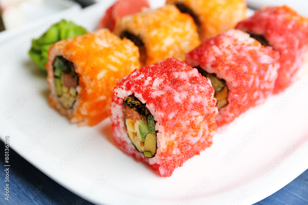 Sushi rolls on plate, chopsticks on color wooden background