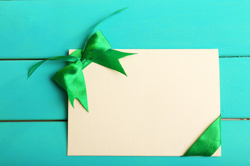 Card decorated with green bow on wooden background