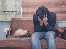 Sad And Depressed Young Man With Cat On Sofa