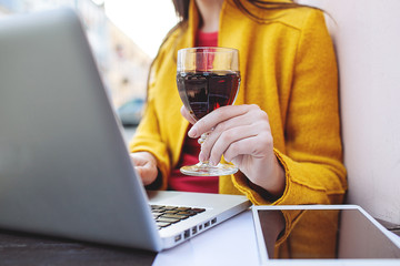 Woman with red wine tablet and laptop in street cafe