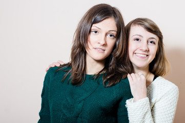 2 young attractive enjoyable women having fun friendly hugging in knitwear happy smiling & looking at camera on white or light copy space background portrait image