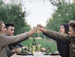 © Mint Images - Group of people toasting with glasses of cider at table in orchard