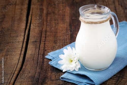 Fotografie, Obraz Fresh milk in a glass jug on a blue napkin with a flower