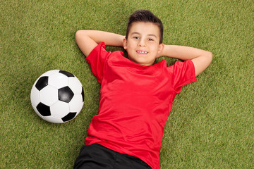 Wall Mural - Carefree boy in a red football jersey lying on grass