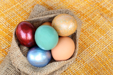 Wall Mural - colorful easter eggs in sack bag on weave background.