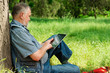 © kostyha - old man sitting under a tree with the tablet