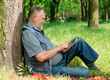 © kostyha - old man sitting under a tree with the tablet